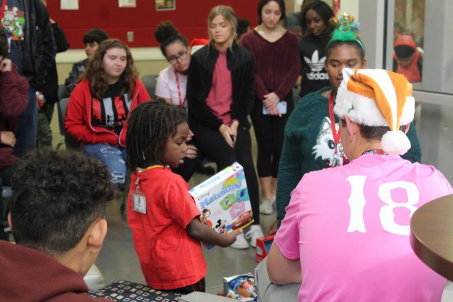 The Pre-K student has a volunteer from one of the many classes that adopted a child to help him unwrap his presents.